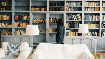 mulher observando os livros em uma sala de casa mobiliada