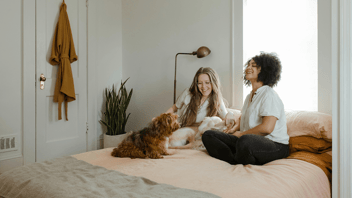 duas mulheres felizes com o seu cachorro na cama