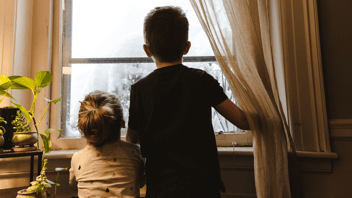 duas crianças olhando pela janela de casa